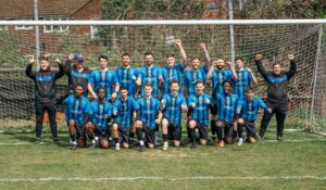 Hinton FC First Team wearing shirts sponsored by Chela, standing within a goal